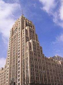 alt=Ground view of a large skyscraper reaching into a blue sky