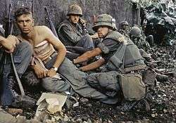 Soldiers waiting nervously with rifles by a wall.